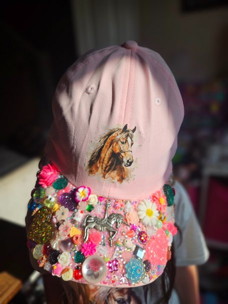 A pink cap adorned with colourful decorations and a horse illustration.